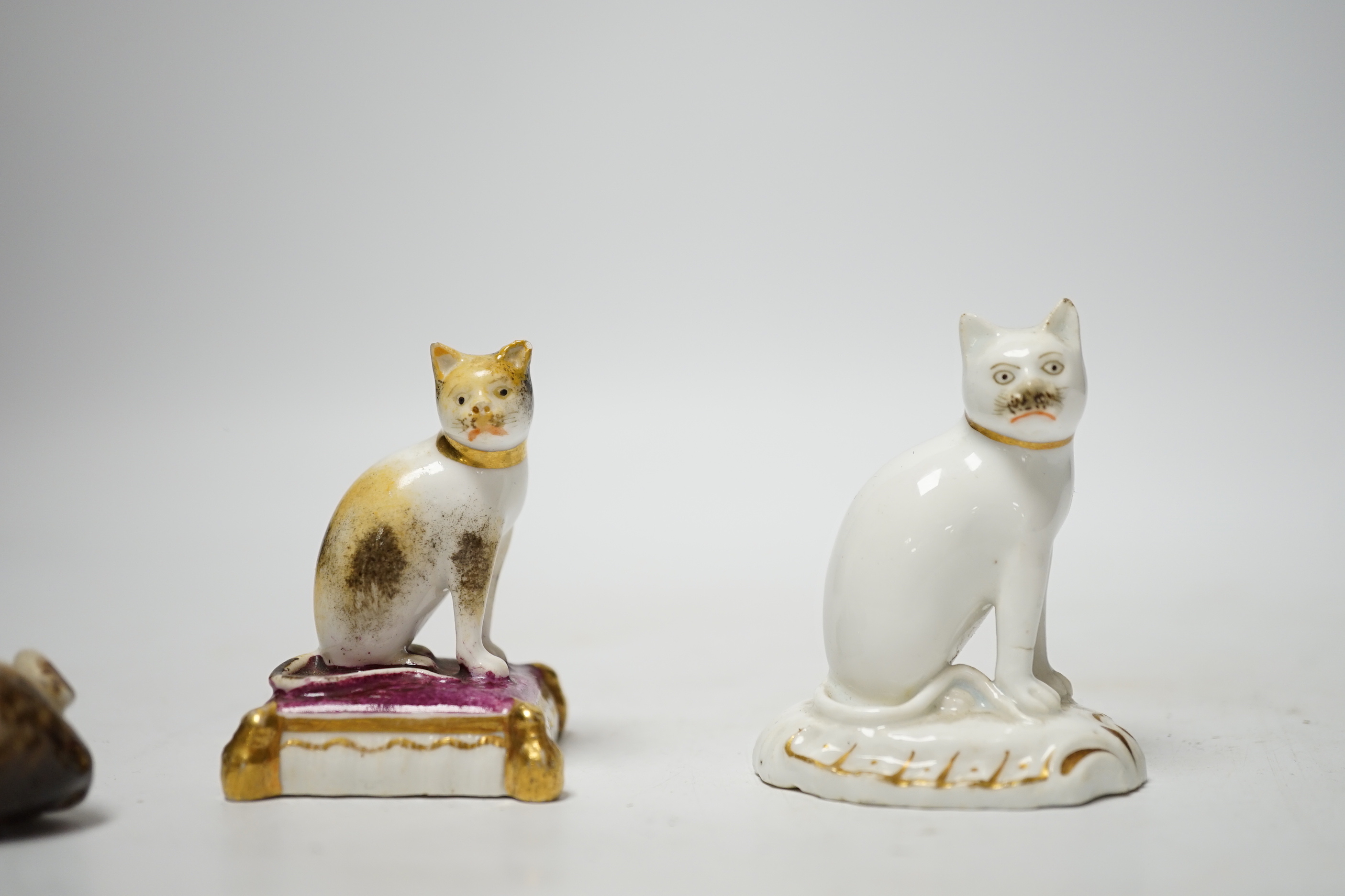 Two Rockingham porcelain models of seated cats, c.1830, the cat seated on a maroon cushion with impressed Rockingham Mark and incised model number 17, 5.3cm high, the white and gilt example with incised model number 11,